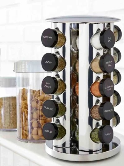 Close-up of a stainless steel masala stand with black caps showing labeled spice jars on a kitchen counter.