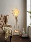 Modern golden tripod floor lamp providing warm aesthetic lighting for drawing room beside an armchair.